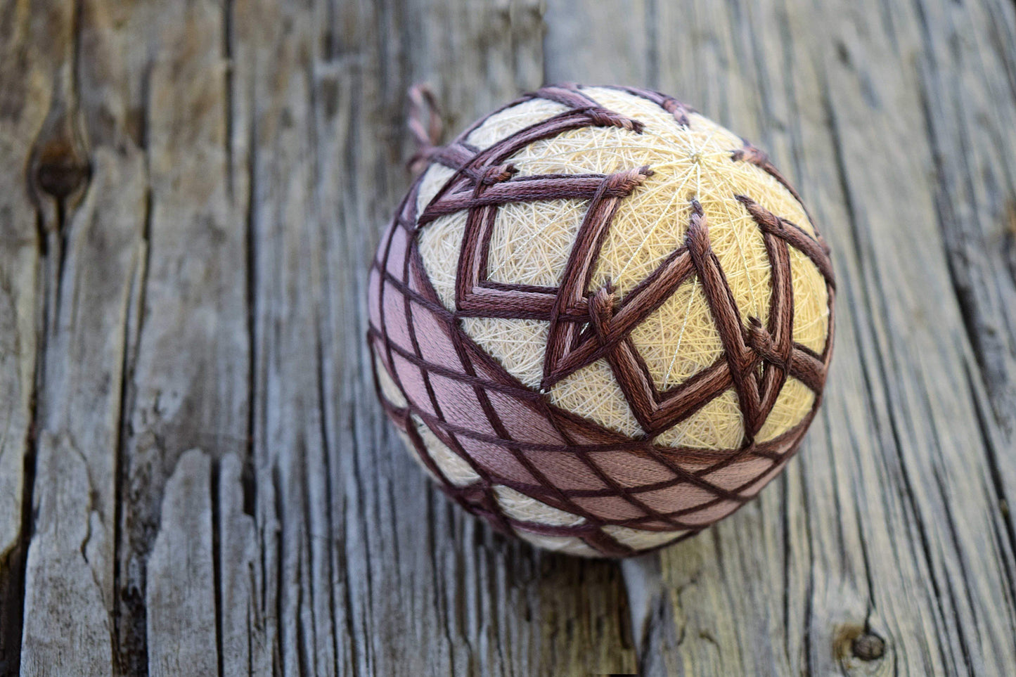 Temari with interwoven flower design in purple on wood