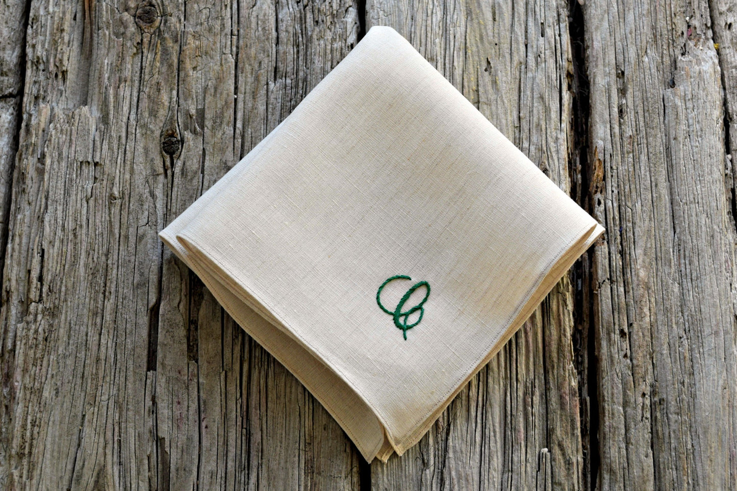 Folded oatmeal linen pocket square with letter embroidered in one corner in green