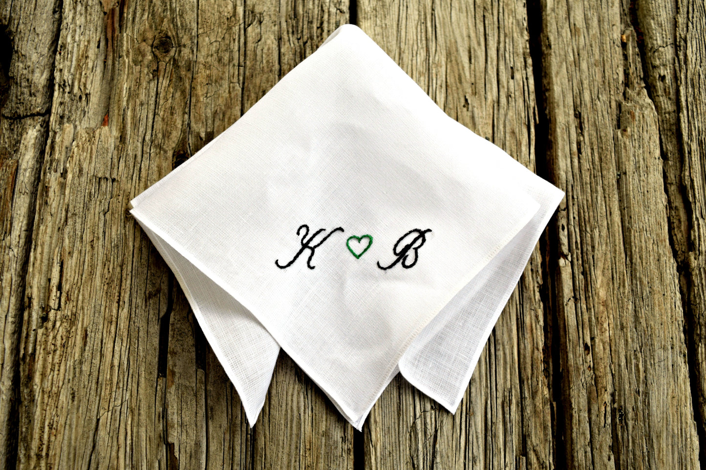 Folded Irish linen handkerchief embroidered with initials on wood ground
