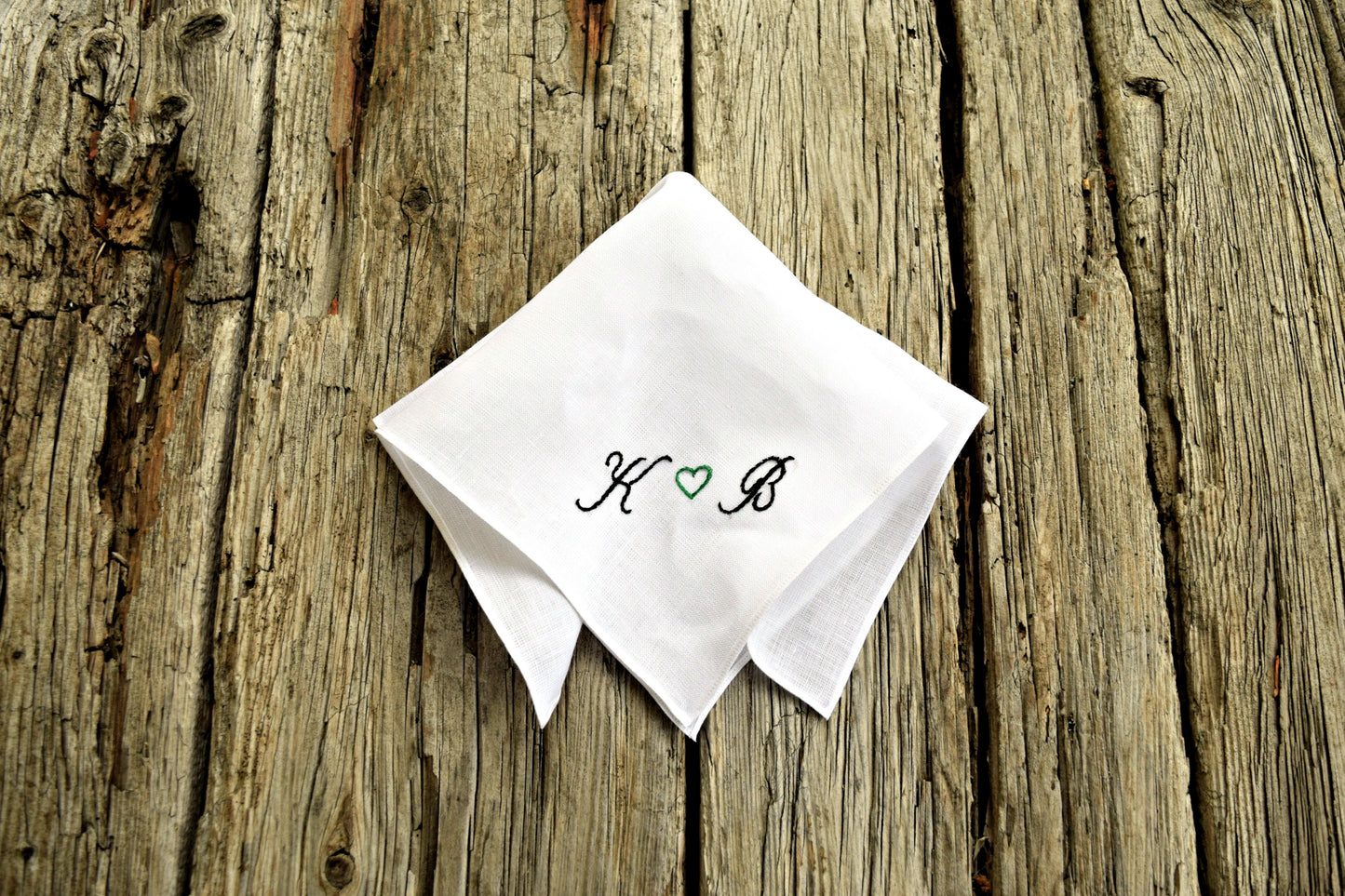 Folded white linen pocket square with initials and heart in copperplate script