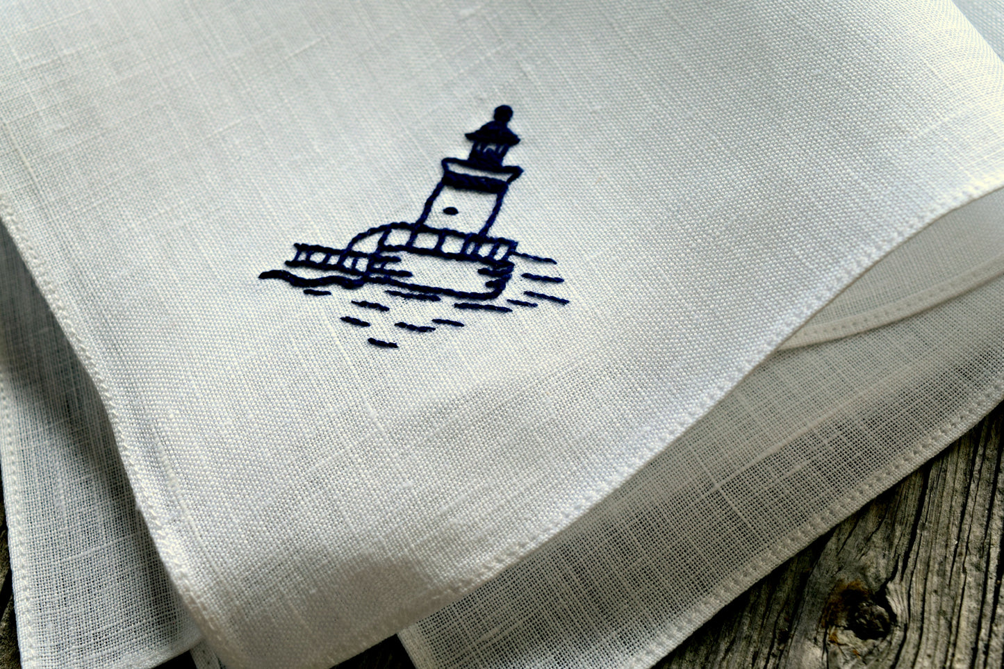 Close up of hand embroidered lighthouse design on white linen handkerchief in navy