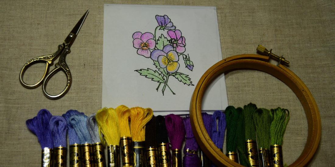 Drawn design of pansies on linen with thread and hand embroidery tools