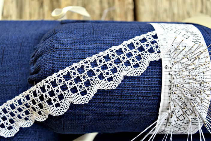 Close up of blue, Princess - style lacemaking pillow with torchon lace edging in progress. Completed lace lays against the pillow and a forest of pins marks current section.
