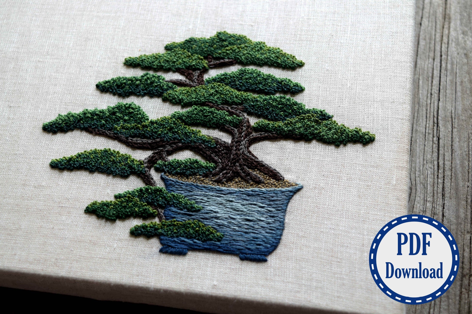 Closeup of hand embroidered juniper bonsai tree with french knot foliage and needlepainted pot. PDF download badge in corner.