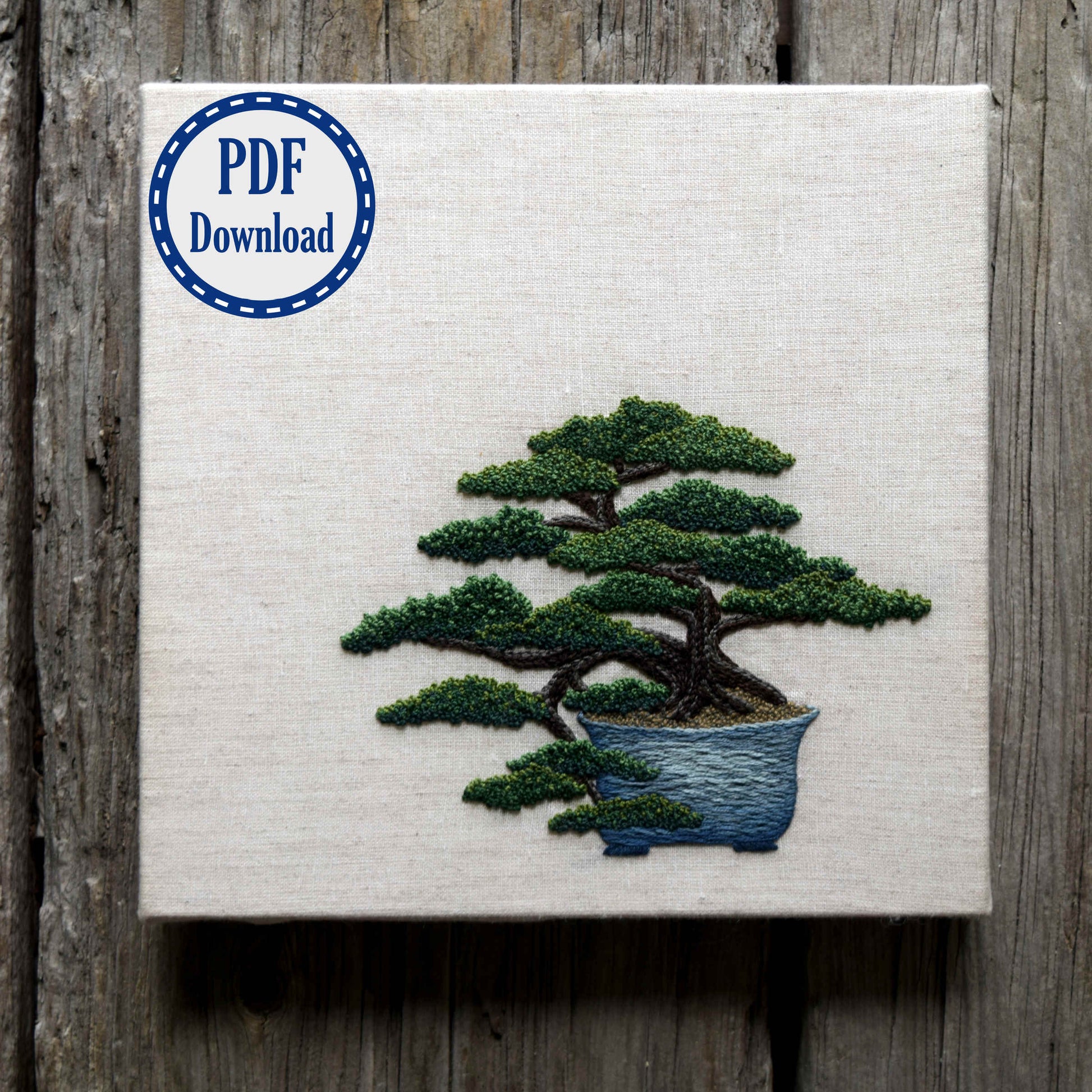 Hand embroidered juniper bonsai in blue pot on natural linen colored fabric. Badge in the corner says PDF download