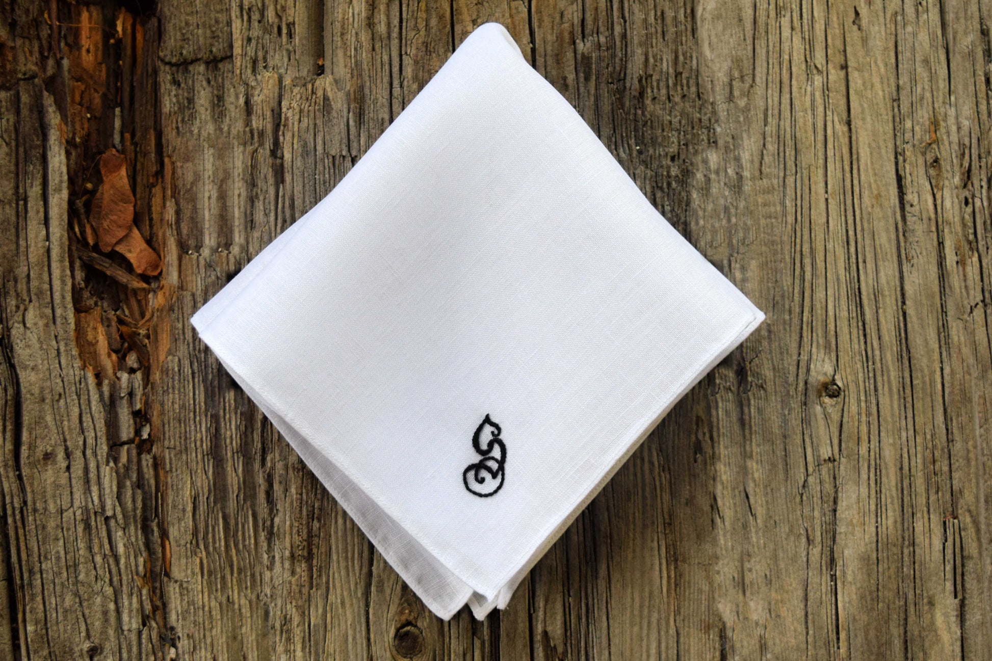 White linen handkerchief with letter s on wood background