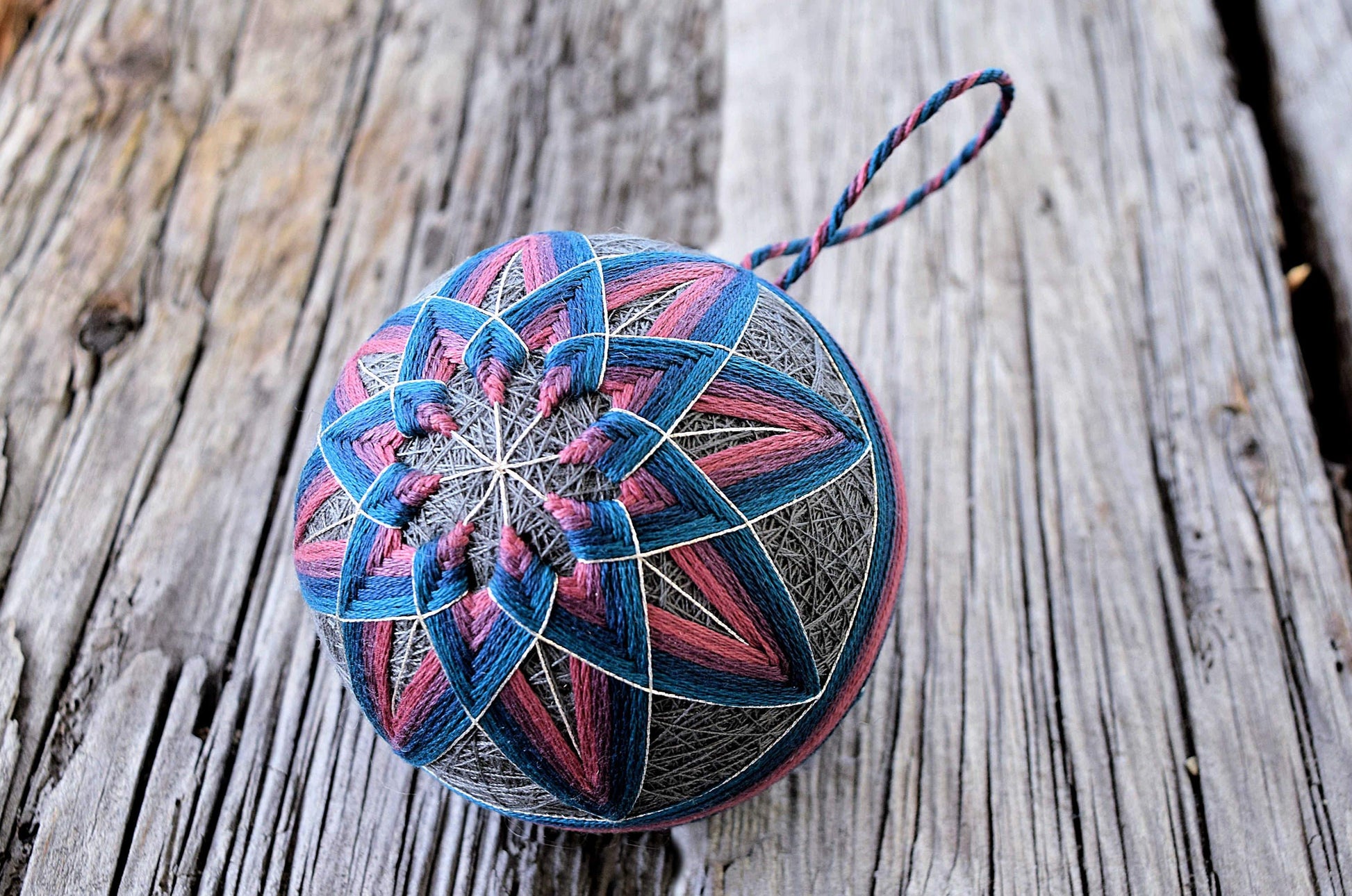 Pink and blue temari ball ornament with kiku design on wood ground