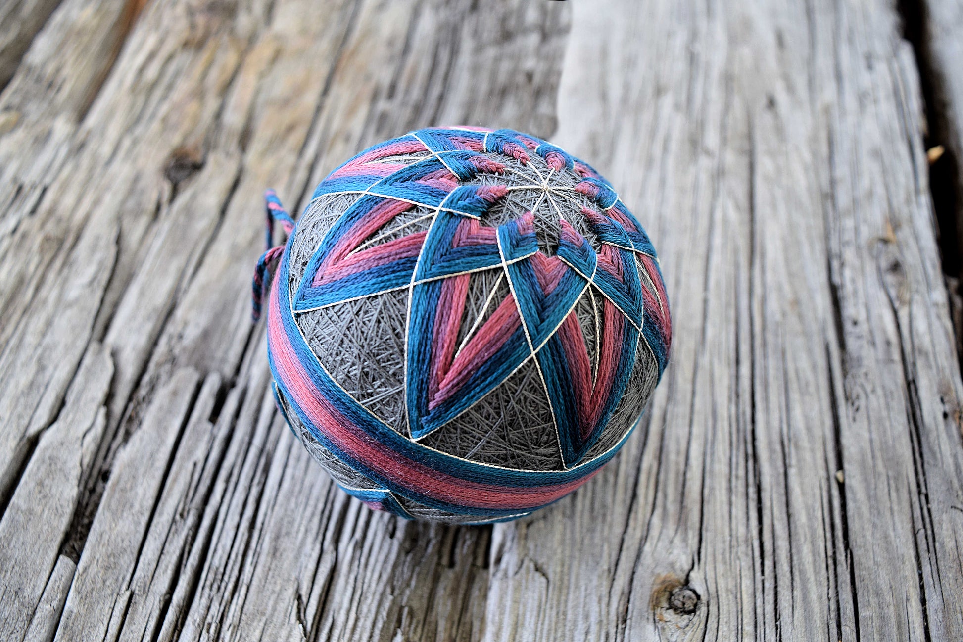 Closeup of pink and blue temari stitched on slate base with wood background