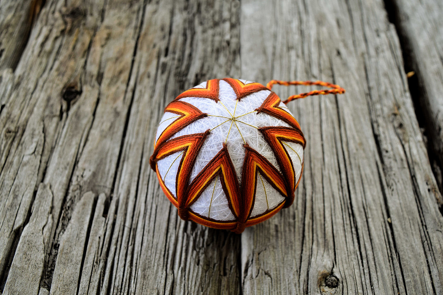 Orange and brown temari ball embroidered in a star pattern on wood background