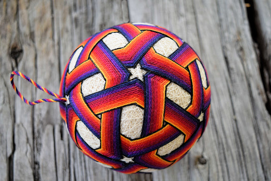 Embroidered temari ball with vibrant bands interlacing to form stars in colors from yellow to deep blue
