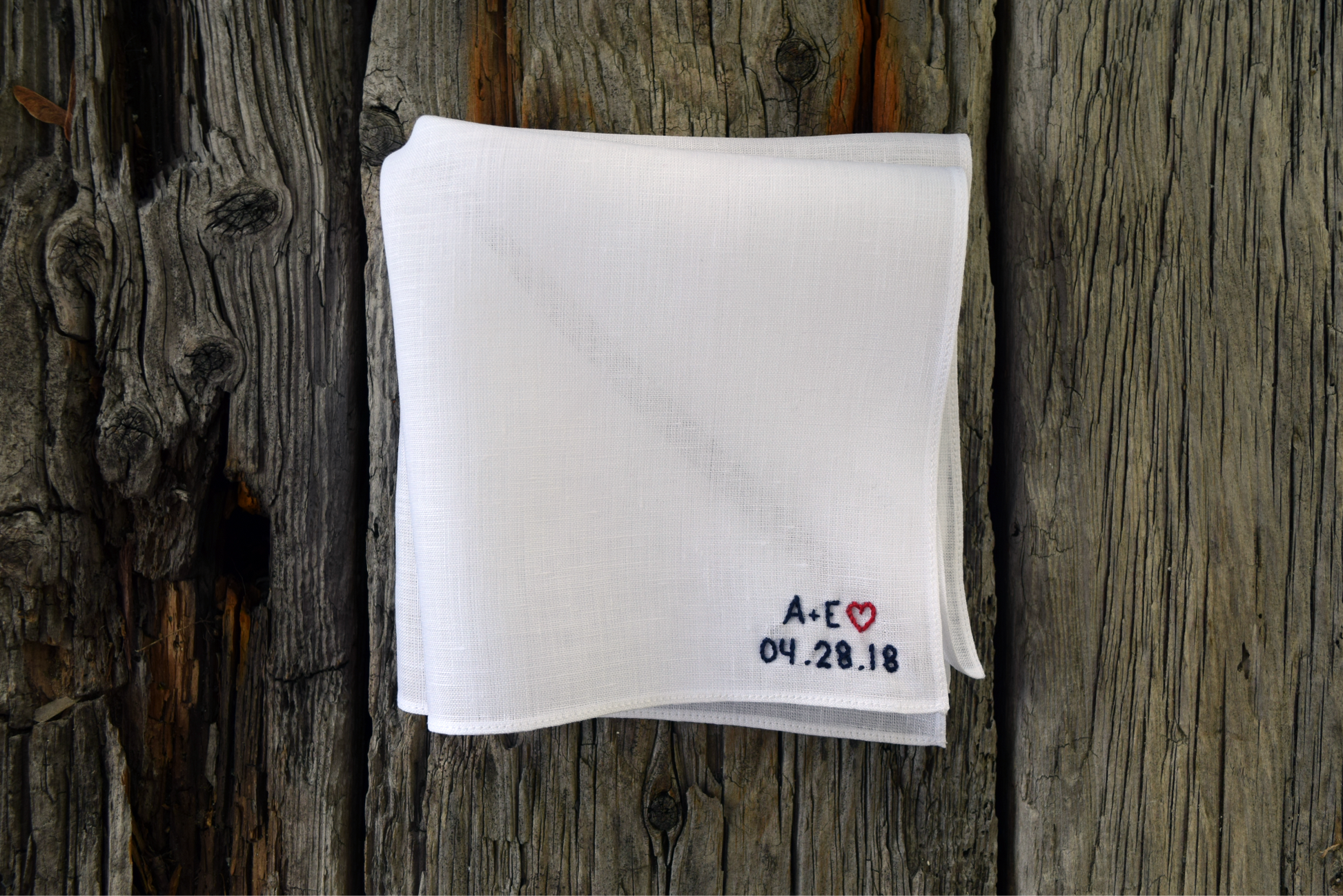 White linen hankie with sweetheart monogram in navy and red on wood background