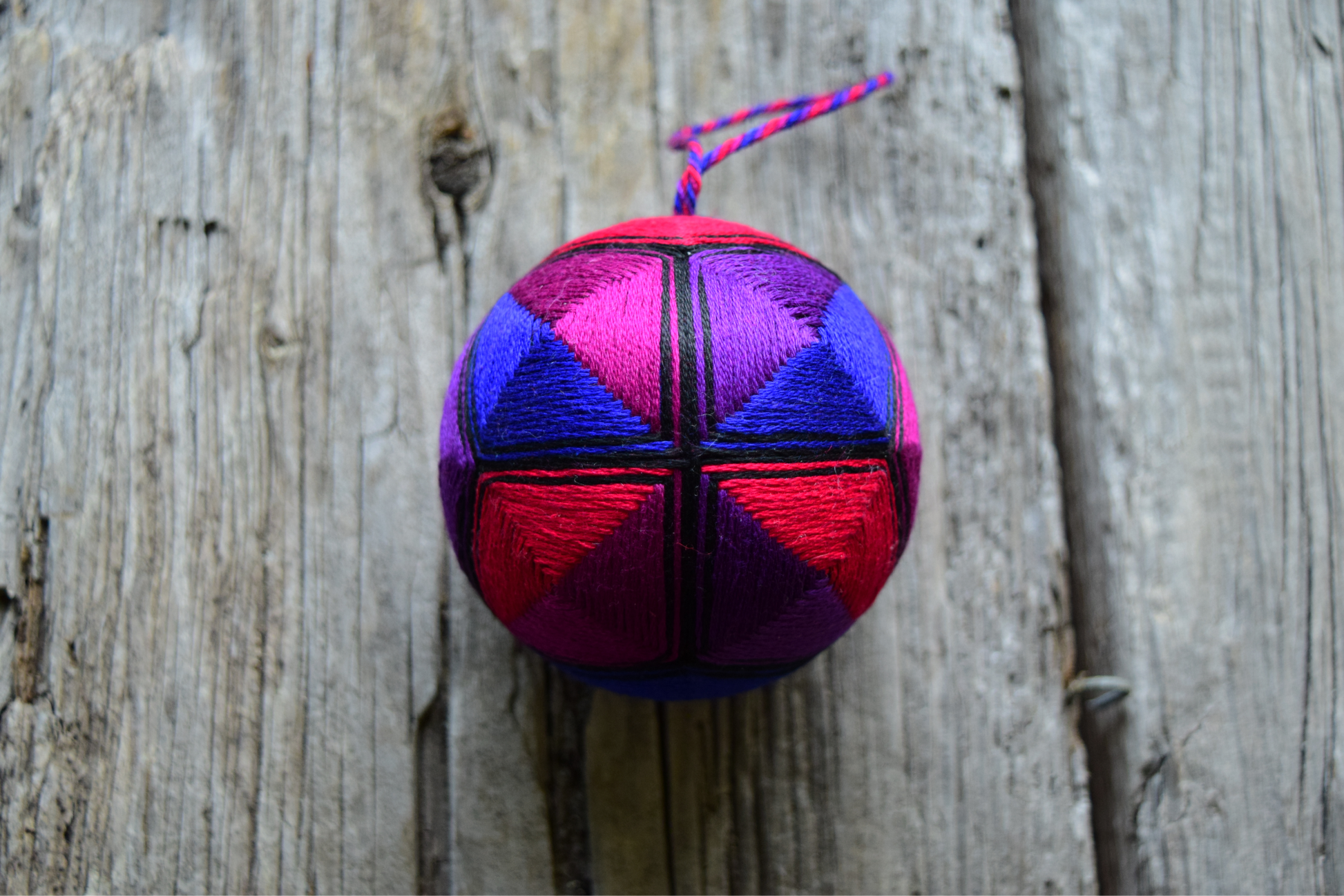 Japanese kousa temari ball stitched in red, purple, blue on wood background