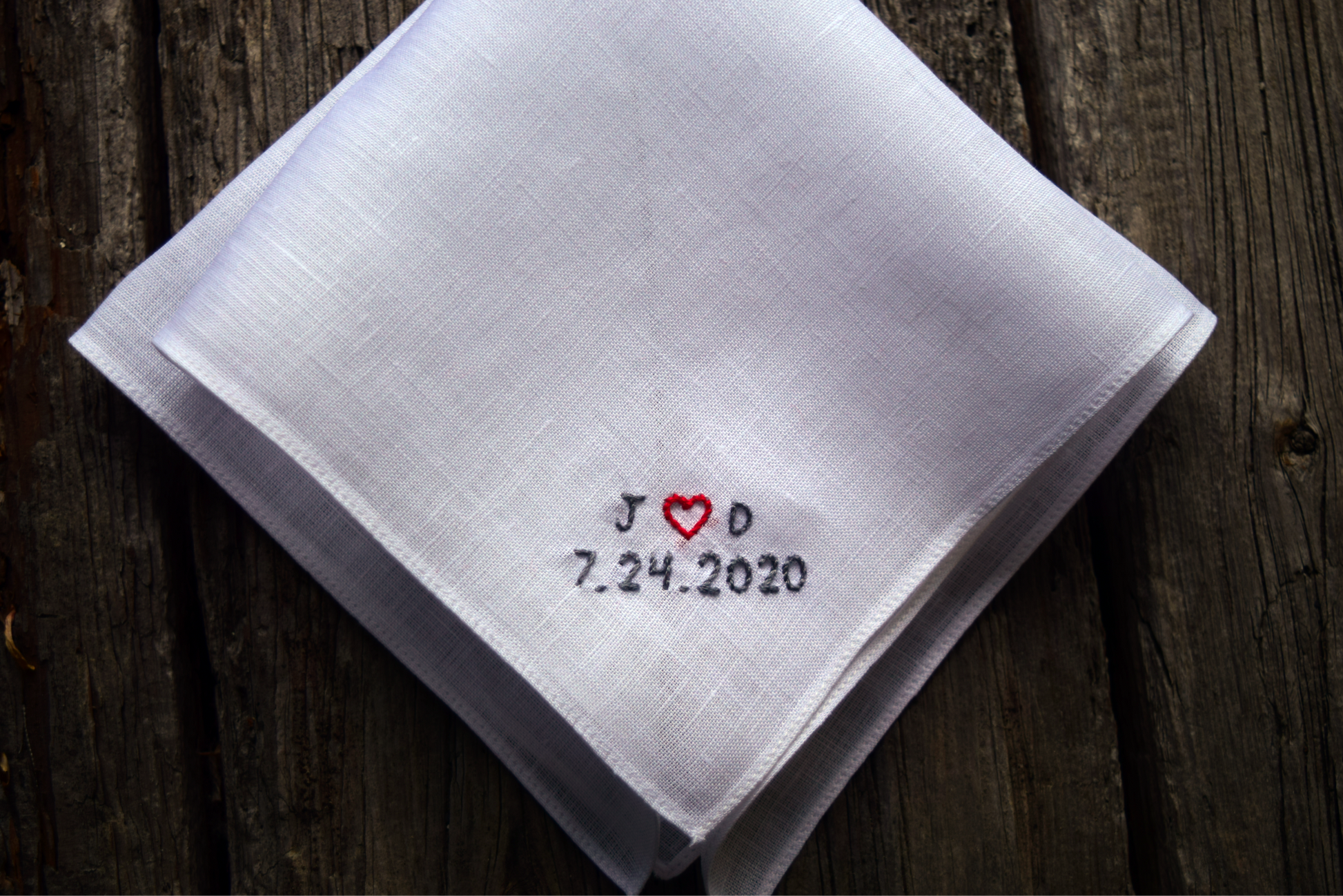 White linen pocket square on wood background embroidered with initials and wedding date