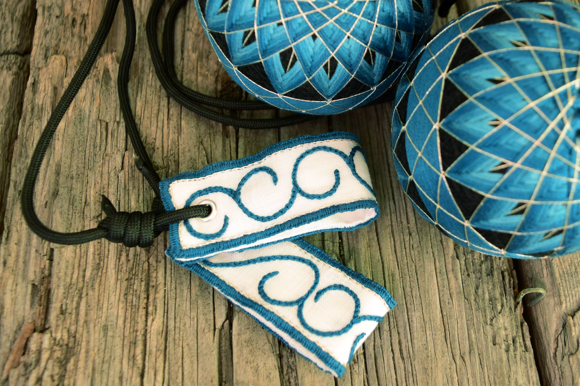 Close up of premium loop embroidered poi handles with teal and silver arabesques