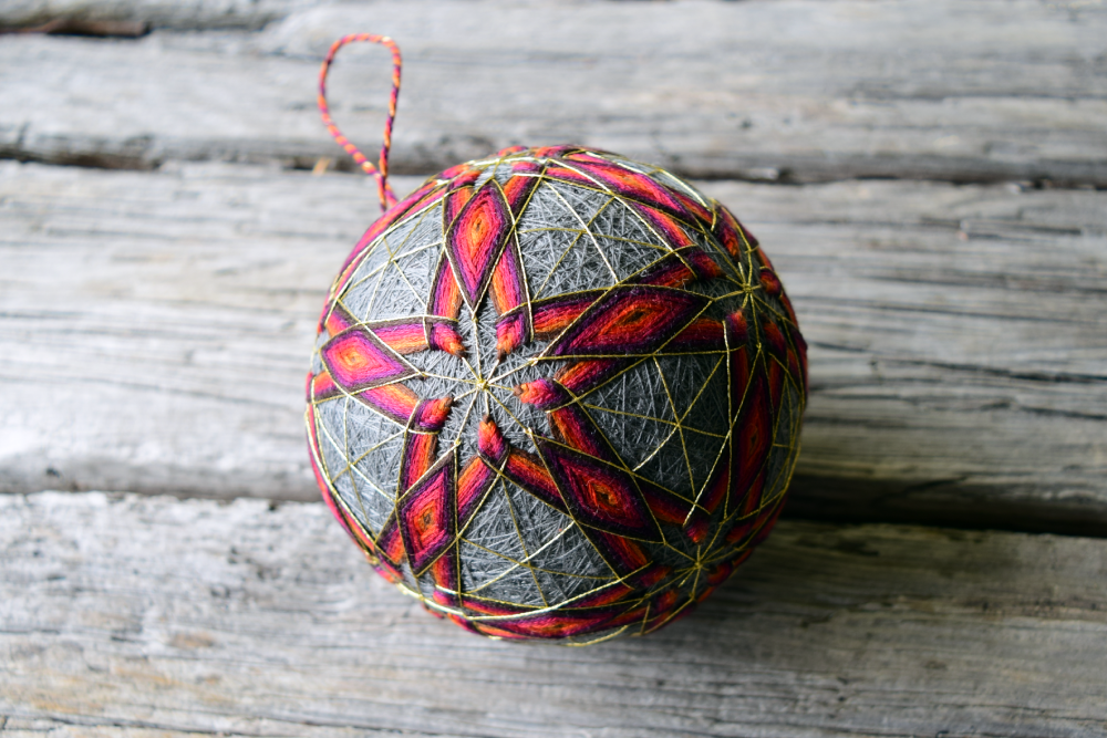Grey temari ball hand embroidered with glowing red and yellow stars