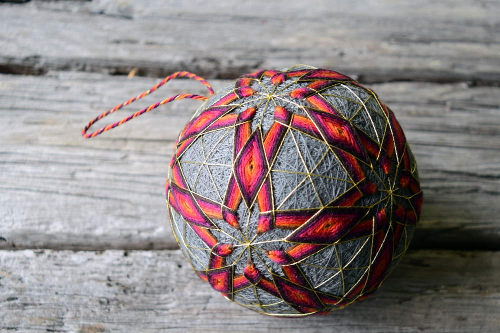 Close up of hand embroidered temari ball with red and brown stars interlocking to form diamonds