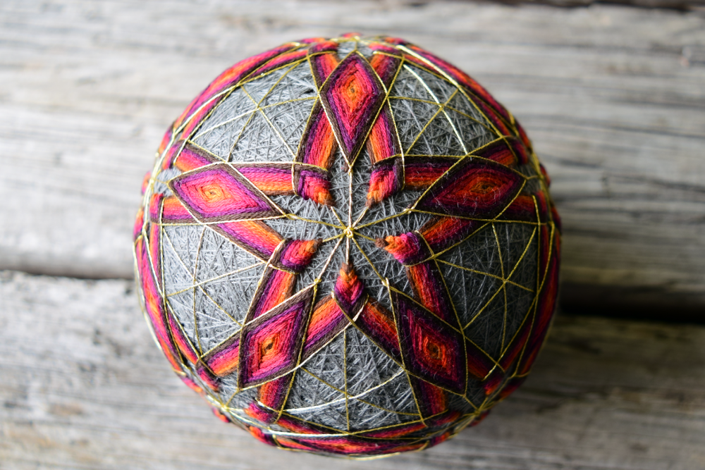 Centered image of star embroidered in warm tones on face of temari ball