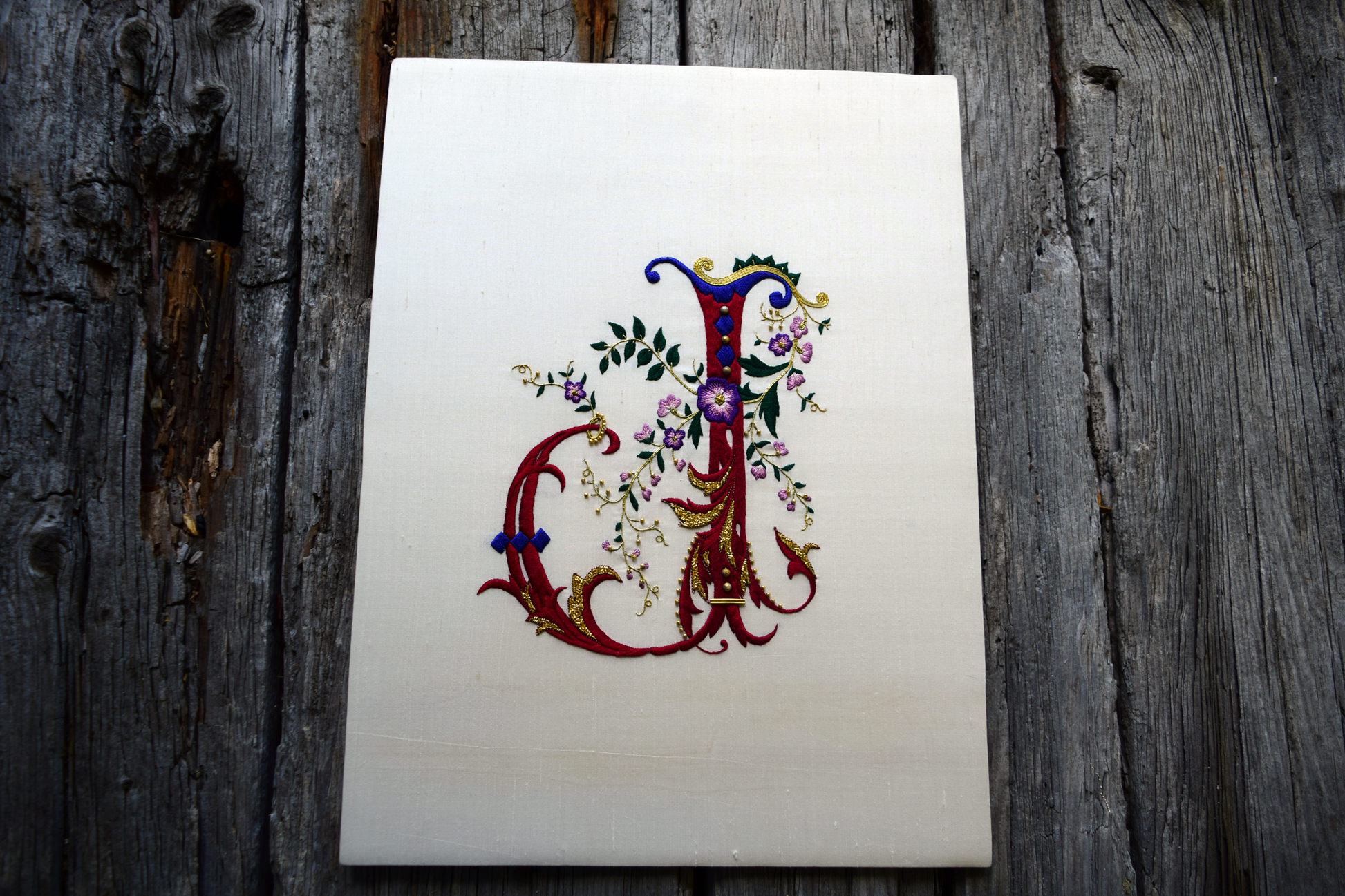 Hand embroidered ornate letter J in red and blue silk with goldwork accents