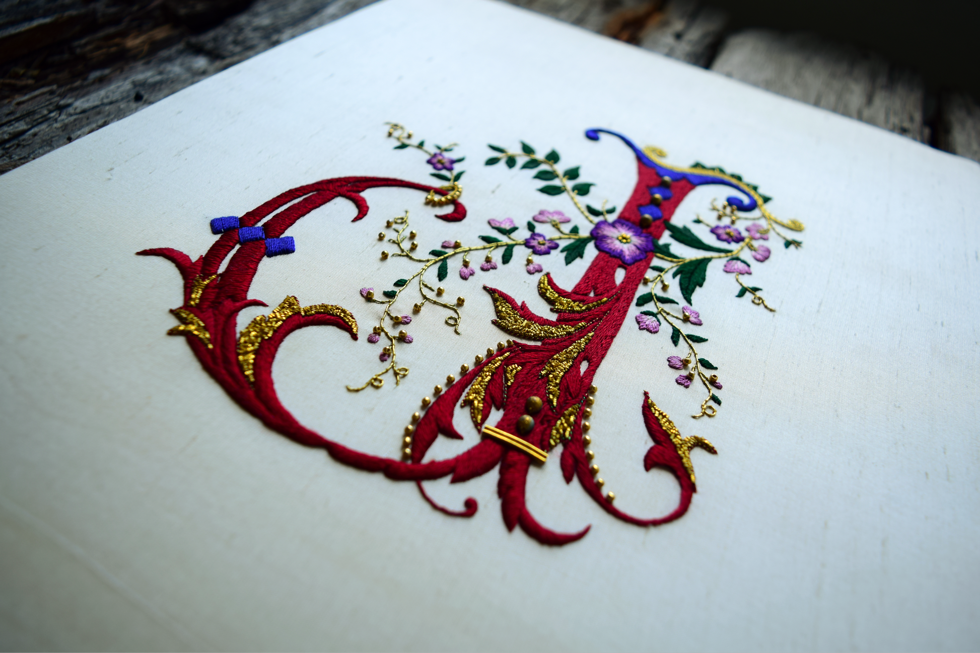 Closeup of hand embroidered monogram in red silk showing goldwork details