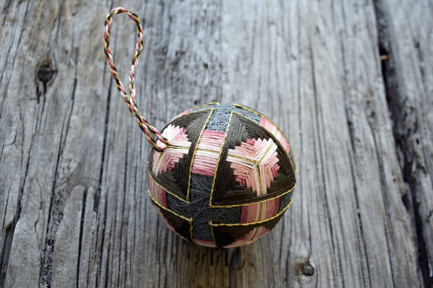 Closeup of hand embroidered temari ball in soft rose and grey browns with twisted thread hanger