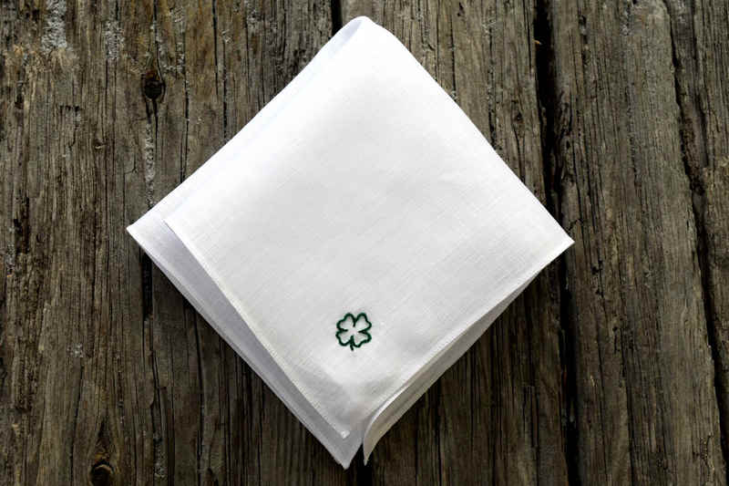 White linen pocket square, folded, showing hand embroidered four leaf clover outline in green