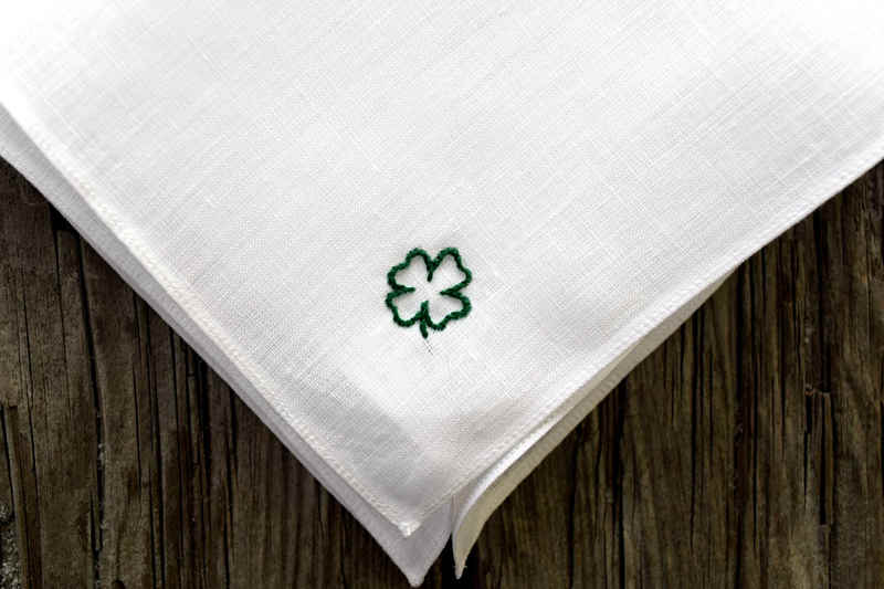 Close up of white linen handkerchief showing small lucky clover design hand embroidered in one corner