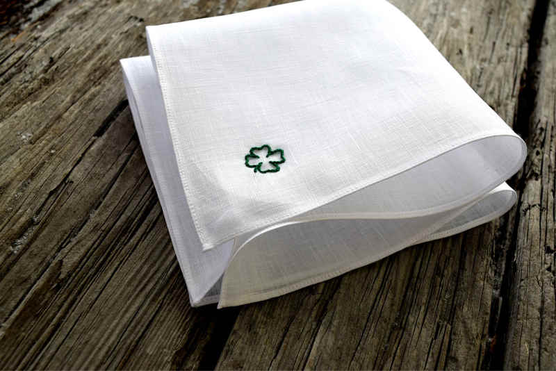 Angled view of white Irish linen handkerchief hand embroidered with a green four leaf clover