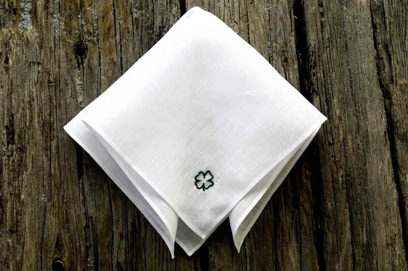 White linen handkerchief, folded, showing embroidered four leaf clover outline in green