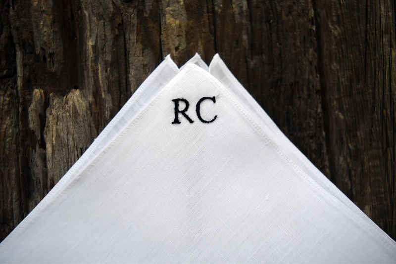 Close up of white linen handkerchief with small block letters in one corner in black