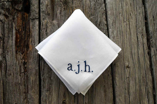 White Irish linen handkerchief hand embroidered with lowercase letters a. j. h. in navy