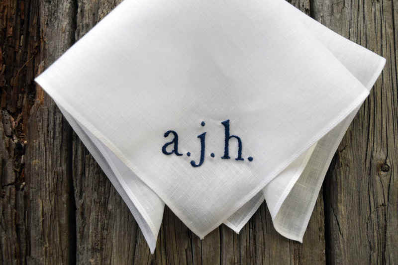 Folded white linen pocket square with hand embroidered initials in one corner. Navy initials are lowercase and read a. j. h.
