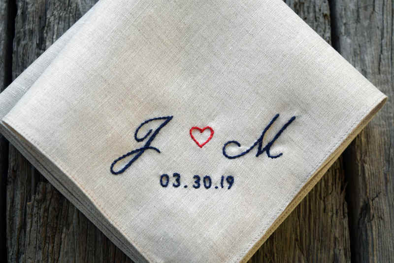 Closeup of natural-color linen handkerchief embroidered with two letters separated by a heart and a wedding date below