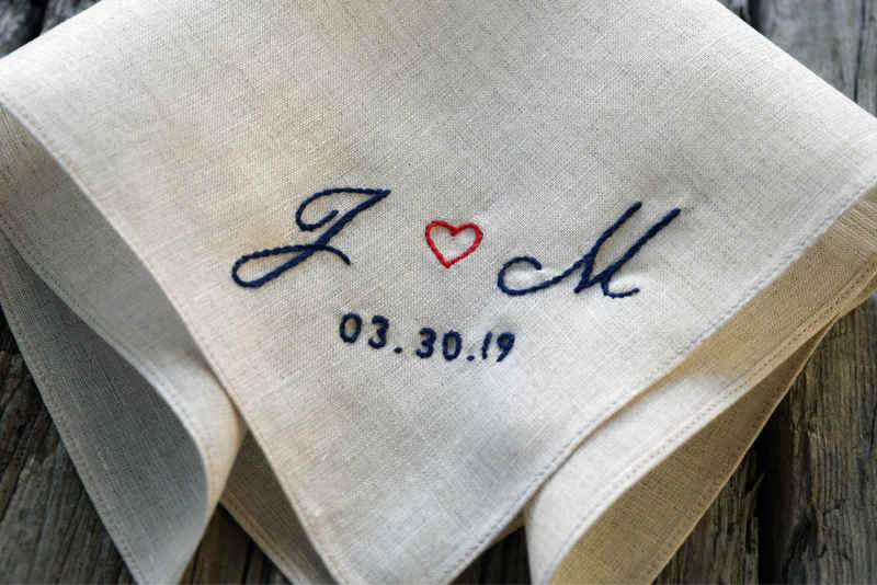 Closeup of oatmeal linen handkerchief with two initials, heart, and wedding date, showing details of navy and red hand embroidered letters