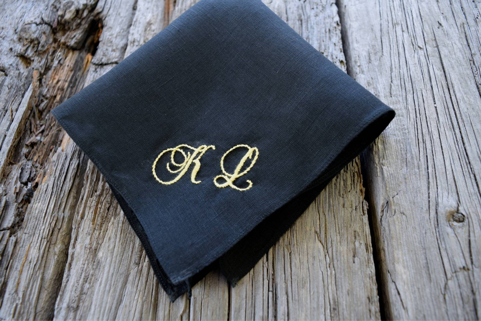 Black Irish linen pocket square hand embroidered with K L in yellow thread on wood background