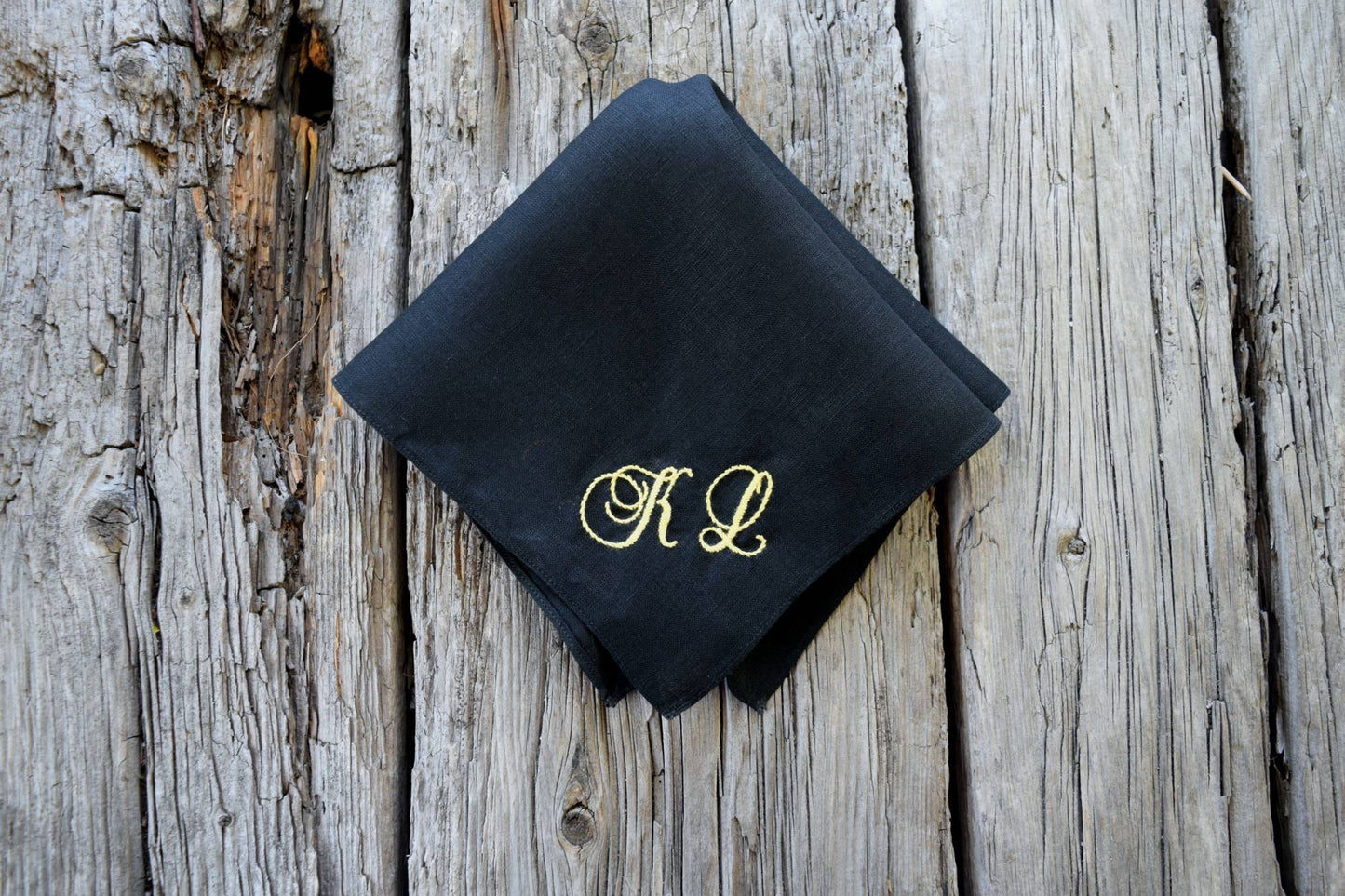 Top down view of black linen hankie personalized with yellow K L in cursive script