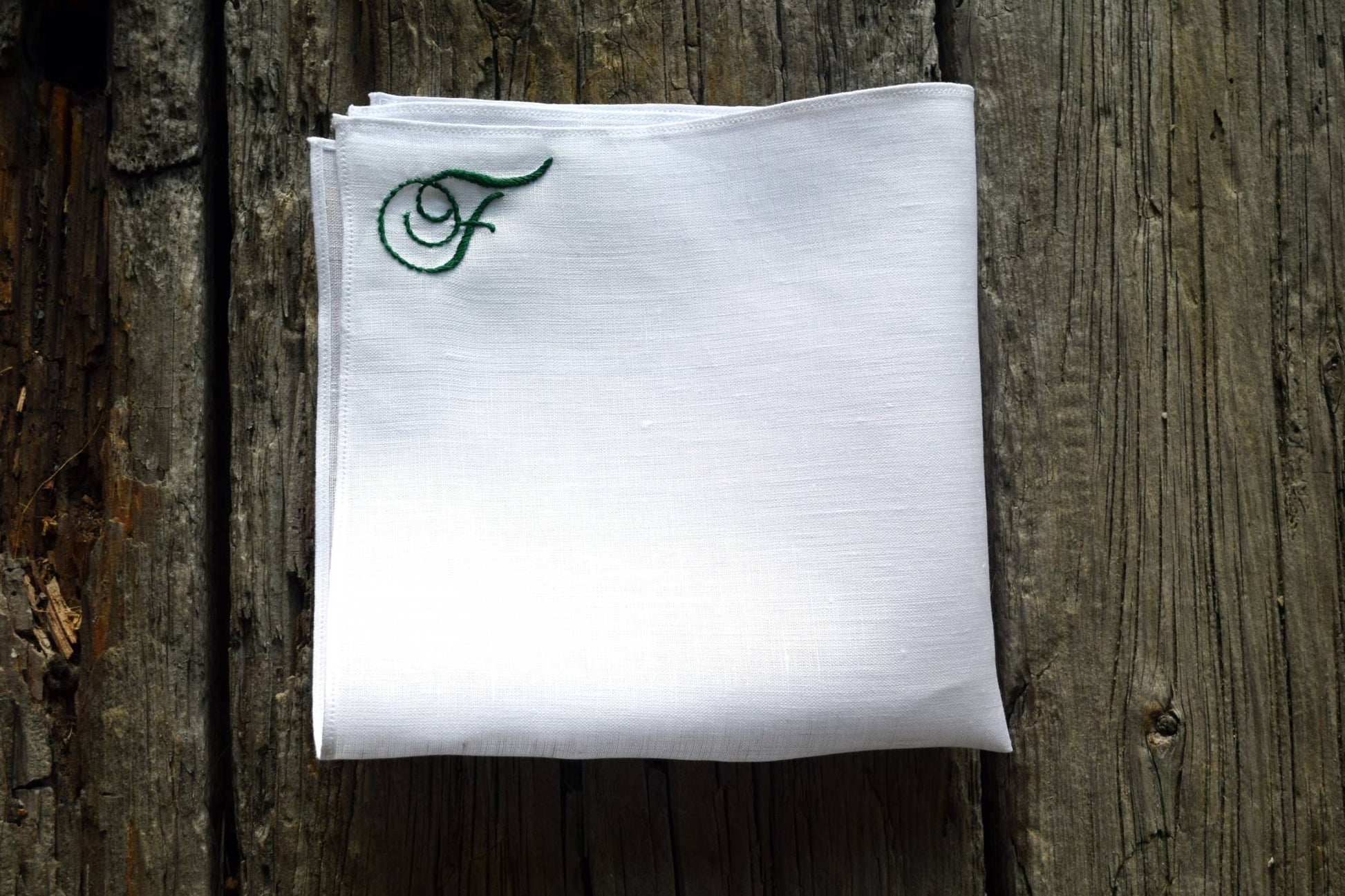 Folded white Irish linen handkerchief with hand embroidered green initial in top corner