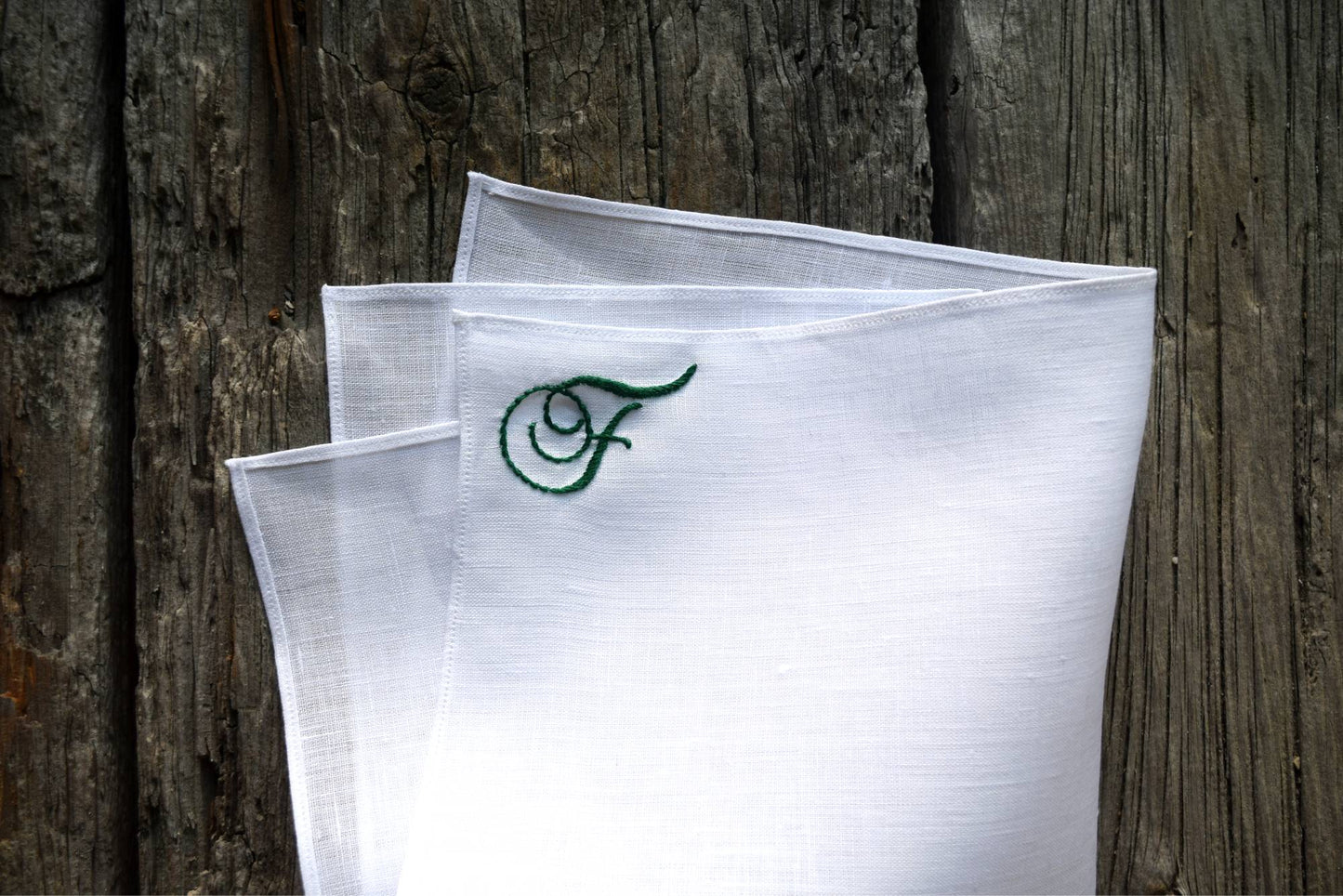 Folded white pocket square hand embroidered with cursive letter F in green