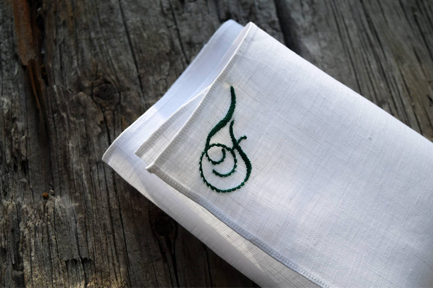 Closeup of white linen handkerchief with scrolled letter F hand embroidered in green