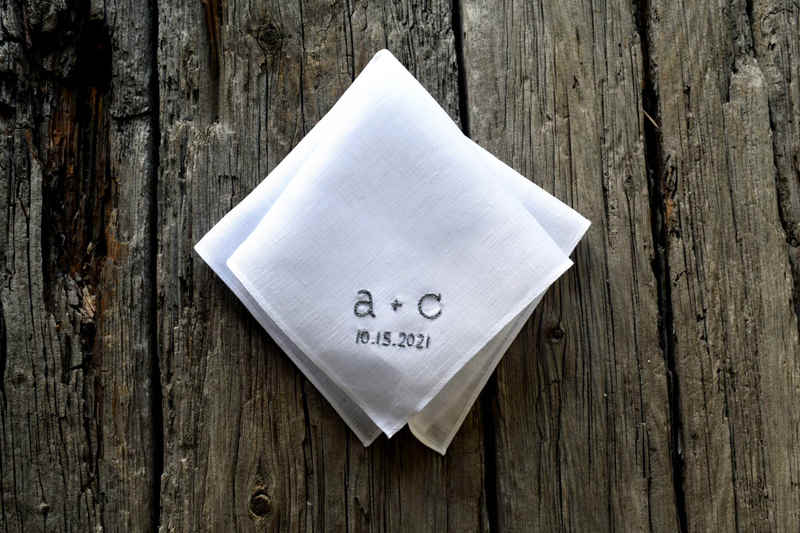 White linen handkerchief, folded, showing a + c 10.15.2021 embroidered in grey in a font like a typewriter