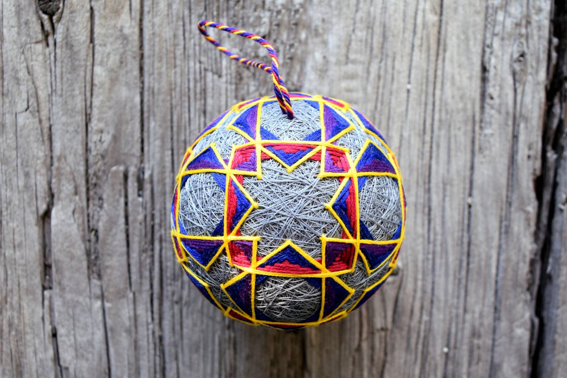 Grey temari ball with geometric design in jewel tones outlined in golden yellow