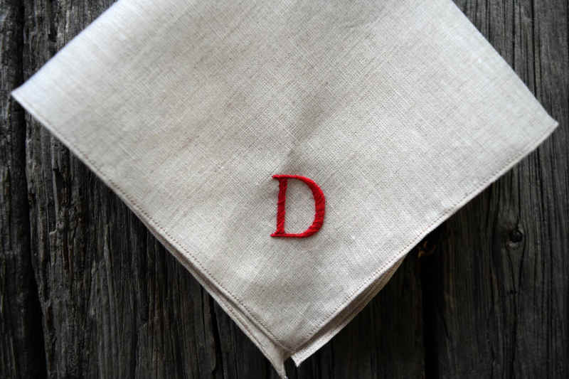 Close up of oatmeal linen handkerchief hand embroidered with red letter D in serif font