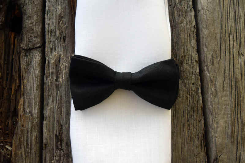 Pre-tied, adjustable black linen bow tie wrapped around white linen pocket square that is folded into a narrow rectangle