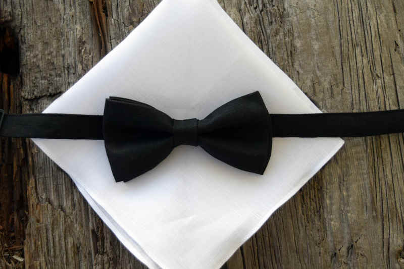 Black linen pre-tied bow tie resting on white linen pocket square