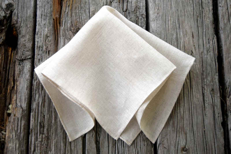 Oatmeal linen handkerchief with hand rolled hem, folded lightly on wood background