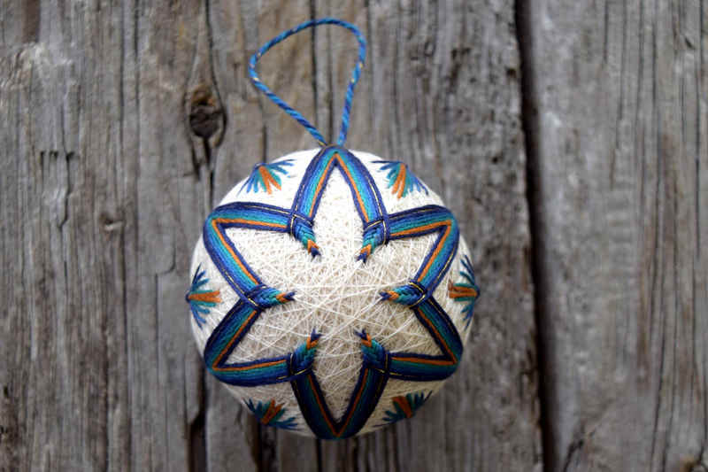 Peacock temari viewed from the center of six-pointed blue, gold, and teal star design. 