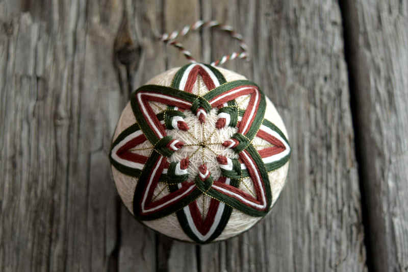 Cream colored temari ball embroidered with forest green and warm brown star design marked out in gold thread