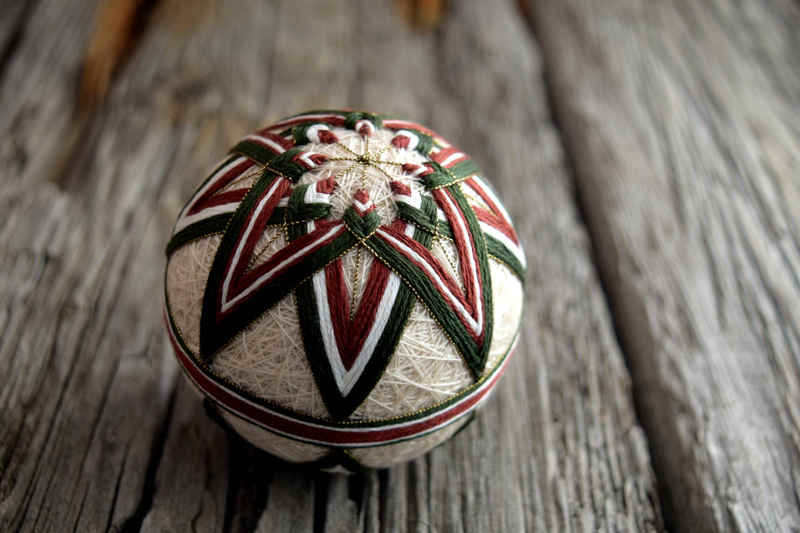 Side view of green and brown temari ball showing points of star and narrow wrapped band around equator of ball