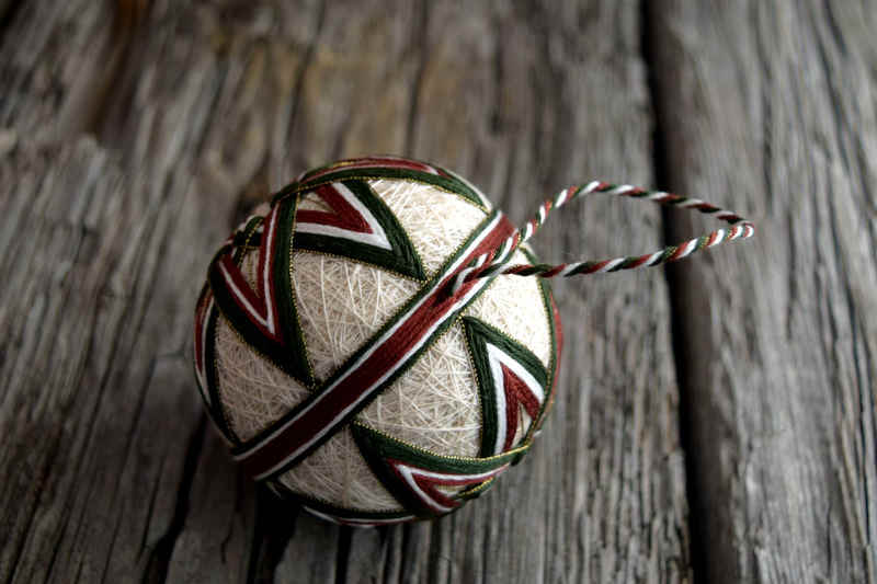 Japanese temari ball embroidered in green and brown kiku design, side view, showing twisted thread hanger and narrow obi band around equator of ball