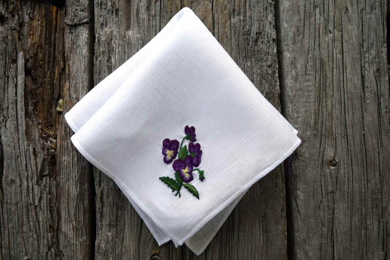 White linen handkerchief embroidered with posy of pansies in purple with yellow centers and green leaves