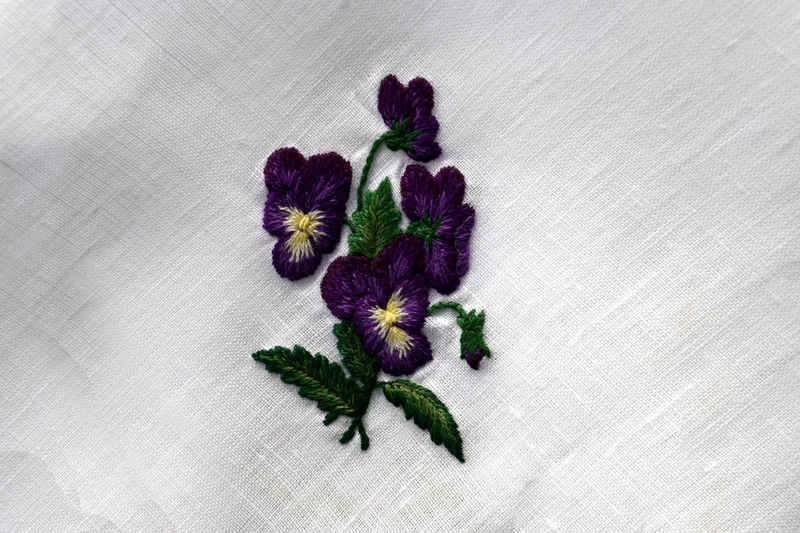Closeup of pansy design showing two pansies open facing the viewer, two open facing away, and a bud. Pansies are purple and leaves are shaded in greens
